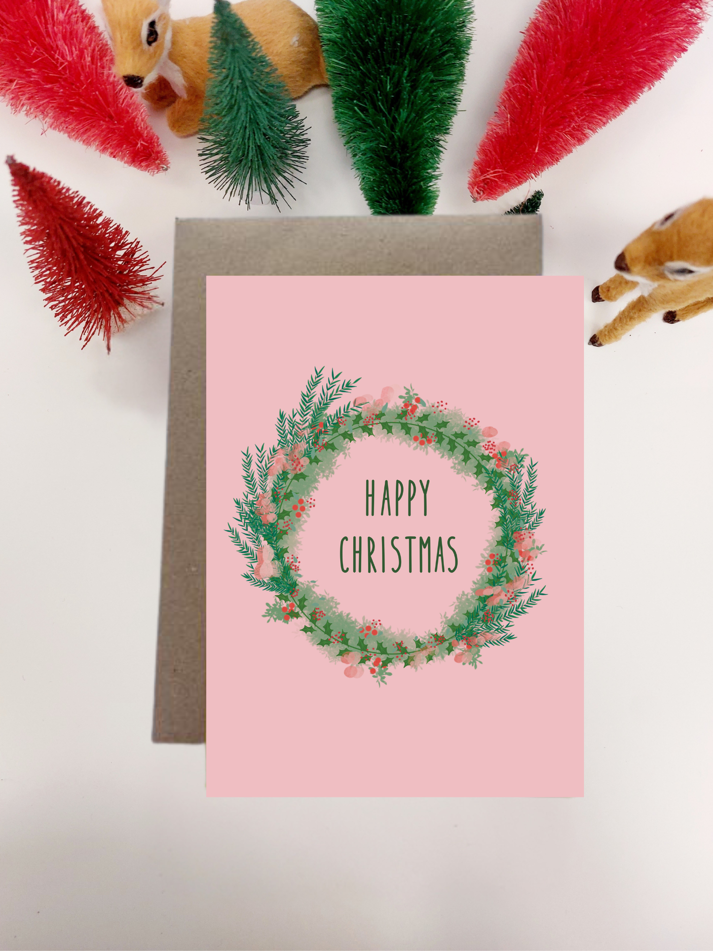 Irish Made Christmas card with wreath design and 'Happy Christmas' text, surrounded by festive decorations on a light background.